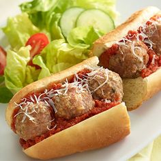 two meatball sub sandwiches on a plate with salad