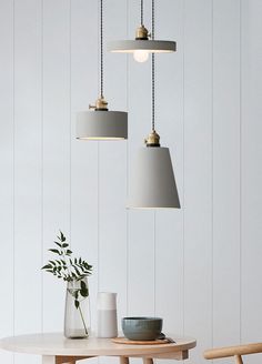 three pendant lights hanging from the ceiling above a table with two vases on it