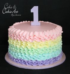 a rainbow cake with the number one on top and icing ruffles around it