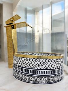 a gold and black vase sitting on top of a white counter next to a golden faucet