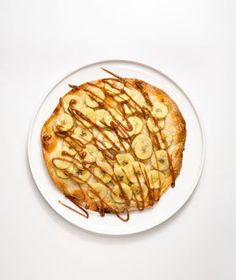 a white plate topped with a pastry covered in bananas and caramel drizzle