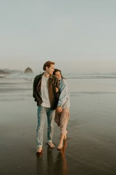 a man and woman walking on the beach with their arms around each other's shoulders