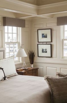 a bed sitting in a bedroom next to two windows with pictures on the wall above it