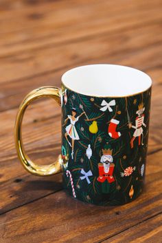 a black and white coffee cup with christmas decorations on it sitting on a wooden table