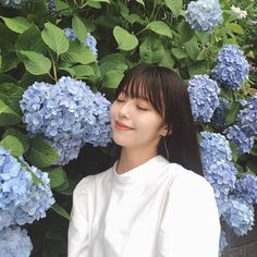 a woman with her eyes closed standing in front of blue hydrangea flowers and smiling