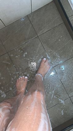 a person's bare feet standing on a tiled floor with water running down them