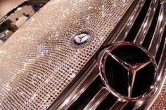 a mercedes emblem on the front grill of a shiny silver car with sequins