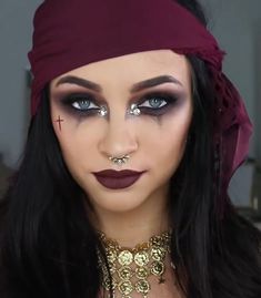 a woman with long black hair wearing a red head scarf and gold jewelry on her face