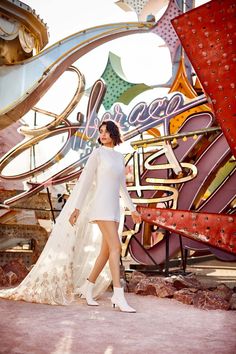 a woman standing in front of a large sign wearing a white dress and high heels