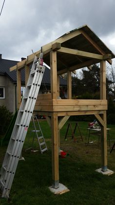 a small wooden structure with a ladder attached to it and a house in the background