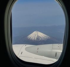 an airplane window with the view of a snow covered mountain in the distance from it