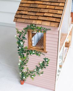 a pink doll house with a window on the roof and greenery growing around it