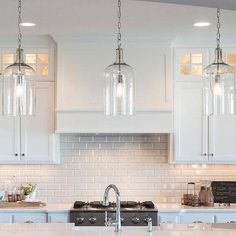 a kitchen with white cabinets and an island in front of the stove top is lit by three pendant lights