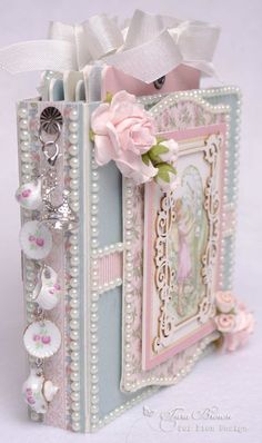 an altered book is decorated with buttons and pearls, flowers, and a pink rose