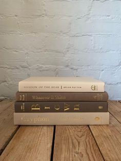 three books stacked on top of each other in front of a white brick wall and wooden table