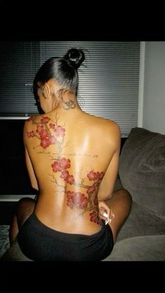 a woman sitting on top of a couch with tattoos on her back and arms behind her head