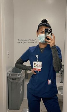 a woman in scrubs taking a selfie with her camera and wearing a face mask