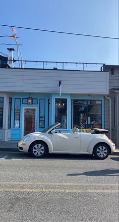 a white convertible car parked in front of a blue and white building on the street