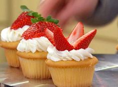 three cupcakes with whipped cream and strawberries on top are sitting on a silver tray