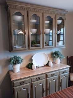 a dining room table with some potted plants on top of it and an old china cabinet