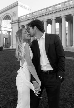 a man and woman kissing in front of an old building with columns on the side