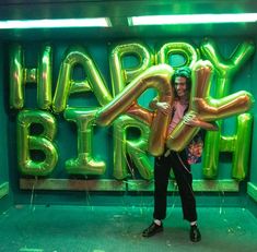 a woman standing in front of a large balloon sign with the words happy birthday written on it