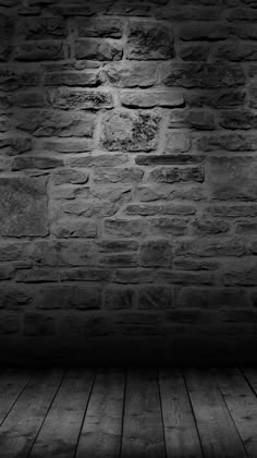 black and white photo of an empty room with brick wall, wooden floor and light coming from above