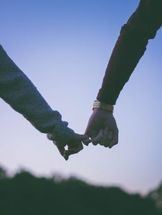 two people holding hands while standing next to each other in front of a blue sky