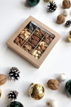 an assortment of nuts in a box surrounded by christmas ornaments and pine cones on a white surface