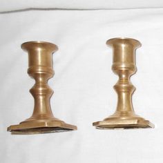 two brass candlesticks sitting side by side on a white sheet