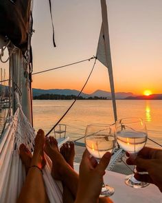 two people sitting on a hammock with wine glasses in their hands at sunset