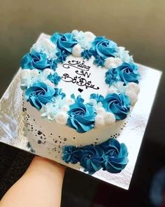 a hand holding a cake with blue and white frosting