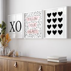 two black and white prints on the wall above a wooden dresser with flowers in vases