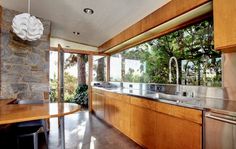 an open kitchen with wood cabinets and stainless steel appliances, along with large windows that look out onto the trees