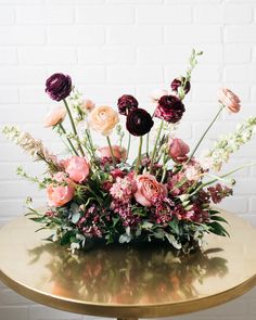 an arrangement of flowers on a table in front of a white brick wall with gold legs