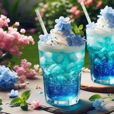 two glasses filled with blue and white liquid on top of a table next to flowers