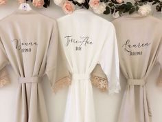 three robes with embroidered names on them hanging up against a wall covered in flowers and greenery