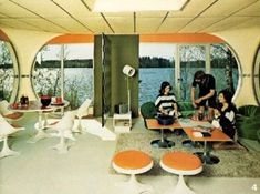 an old photo of people sitting in a living room with large windows looking out onto the water