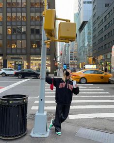 a woman is crossing the street in front of a traffic light and trash can on the side of the road