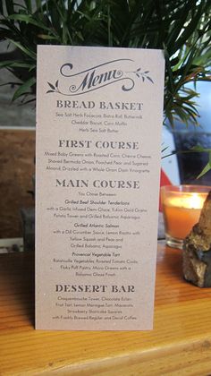 a menu sitting on top of a wooden table next to a candle and potted plant