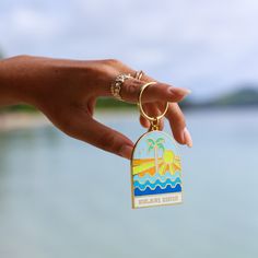 a hand holding a keychain with a beach scene on it and the ocean in the background