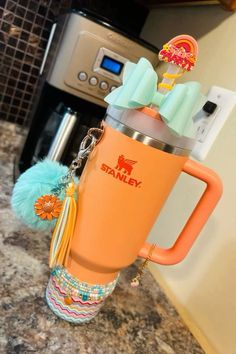 an orange travel mug with tassels and keychain hanging from the handle