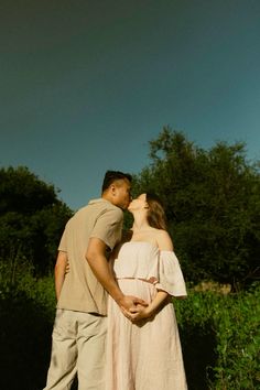 a man and woman standing next to each other in front of some bushes, kissing