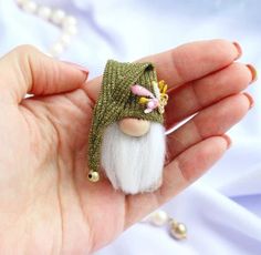 a hand holding a small doll with a green hat on it's head and white hair