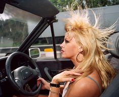 a woman sitting in the driver's seat of a car with her hair blowing in the wind