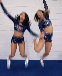 two women in sequins are dancing on a blue carpet with white bricks behind them