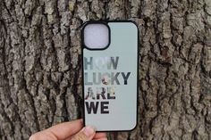 a person holding up a phone case that says how lucky are we in front of a tree