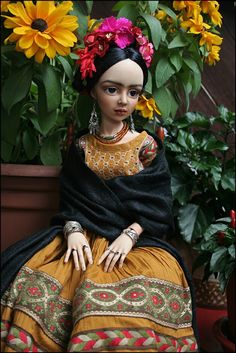 a doll sitting in front of a potted plant with sunflowers on it