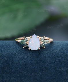 a white opal and green tourmaline ring sitting on top of a blue cloth