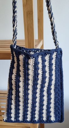 a crocheted blue and white bag hanging from a wooden chair next to a wall